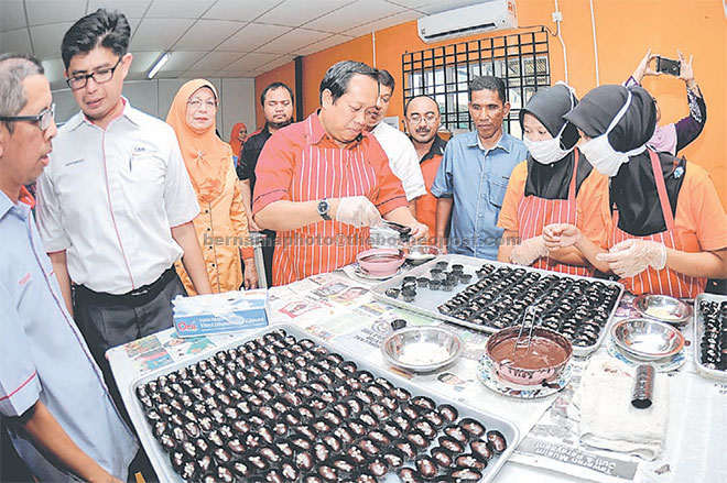  Ahmad Maslan (tengah) meletakkan biskut coklat ke dalam bekas sewaktu meninjau pembuatan biskut selepas merasmikan kilang biskut RMT Timur Qaseh Sdn Bhd di Ajil, semalam. — Gambar Bernama