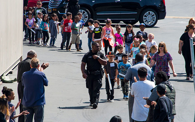  Seorang pegawai polis mengetuai barisan pelajar sekolah yang akan diserahkan kepada ibu bapa masing-masing sejurus selepas kejadian berdarah di San Bernardino, California kelmarin. — Gambar AFP