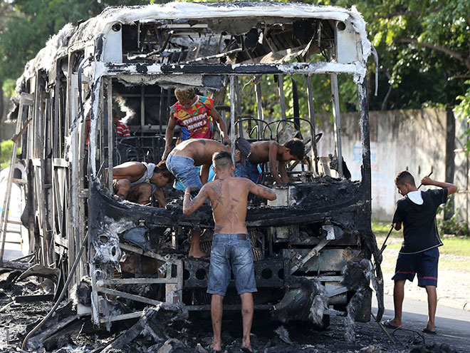  Orang ramai dilihat menanggalkan rangka bas yang rentung di Fortaleza, Brazil kelmarin. — Gambar Reuters