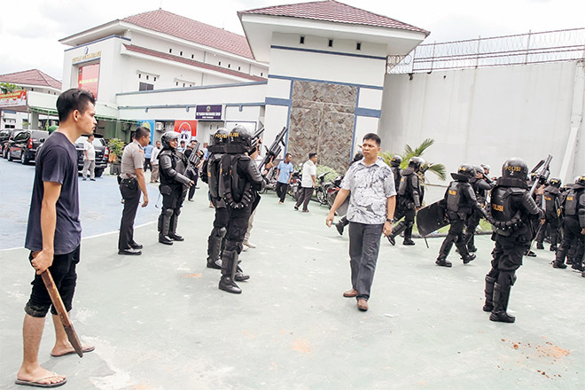  Seorang penduduk kampung (kiri) yang tinggal berhampiran dan anggota polis antirusuhan bersenjatakan raifal berkawal di depan kompleks Penjara Sialang Bungkuk dalam gambar rakaman Antara Foto kelmarin. — Gambar Reuters