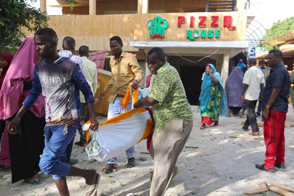  Tiga lelaki mengangkat mayat mangsa terbunuh dalam serangan di sebuah restoran di Mogadishu, semalam. — Gambar Reuters