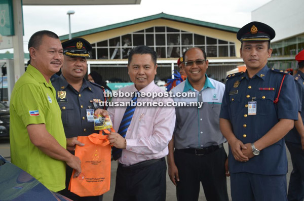  Alijus menyerahkan pelekat dan cenderamata kepada seorang pengguna jalan raya sempena kempen yang dijalankan, sambil diperhatikan oleh Ismaidi dan pegawai-pegawai Bomba Zon Tawau yang hadir.