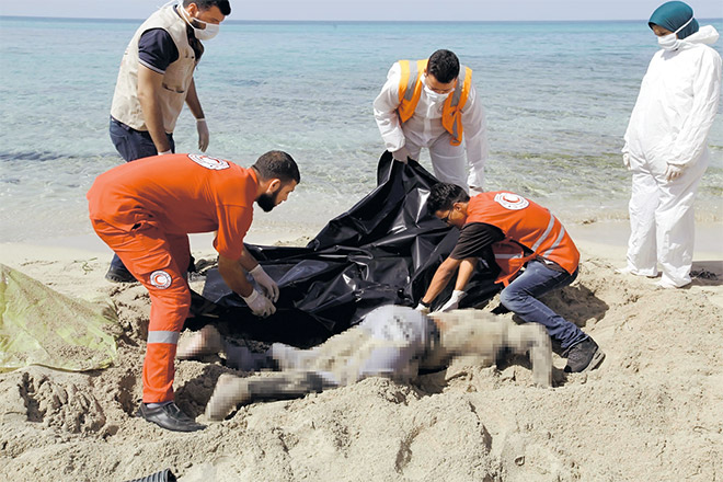  Penyelamat menutup mayat pendatang dengan beg plastik di pantai timur Tripoli, Libya kelmarin. — Gambar Reuters