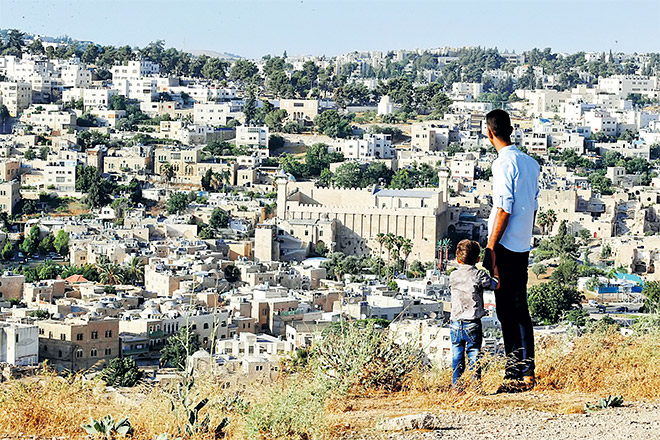  Seorang lelaki Palestin dan anaknya kelmarin melihat penempatan haram peneroka Yahudi yang melatari Tebing Barat, Hebron. — Gambar Reuters