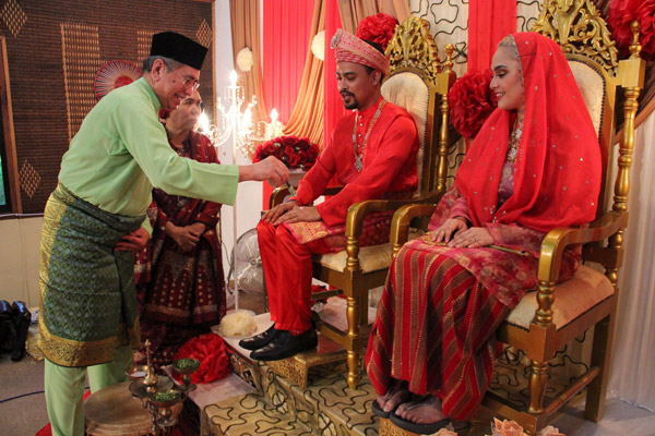  Junaidi (kiri) merenjis pasangan pengantin olok-olok bagi menghidupkan budaya Melayu pada Majlis Indahnya Raya Homestay Kampung Santubong. 