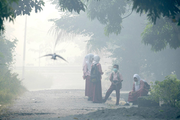  Pelajar sekolah di Aceh memakai topeng muka ketika menunggu bas sekolah. Aceh berasap tebal ekoran kebakaran hutan tanah gambut di Meulaboh, kelmarin. — Gambar AFP