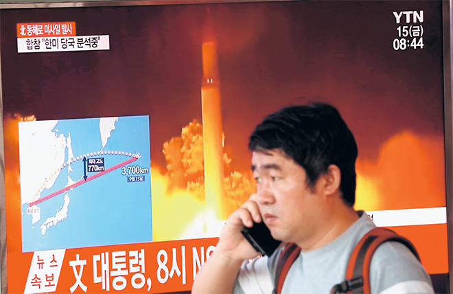  Seorang lelaki melintasi skrin televisyen yang melaporkan mengenai pelancaran misil balistik Korea Utara melalui Jepun ke Pasifik, di Seoul semalam. — Gambar Reuters