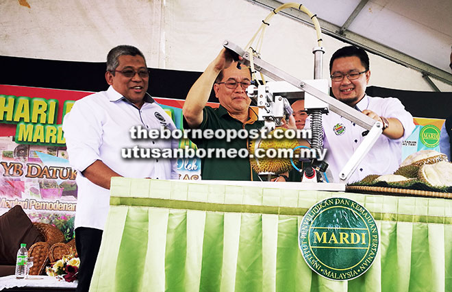  Uggah (tengah) membuka buah durian menggunakan mesin yang dicipta khas sebagai simbolik Majlis Perasmian Hari Bersama Pelanggan MARDI Sarawak 2017 di pejabat MARDI Sarawak di Kuching semalam. Turut kelihatan Sharif (kiri).