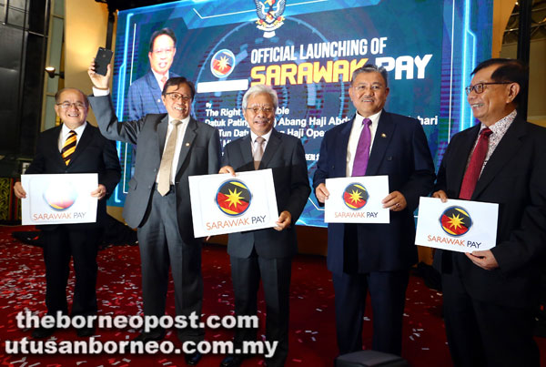  Abang Johari (dua kiri) menunjukkan telefon bimbit yang menandakan aplikasi Sarawak Pay kini boleh dimuat turun dalam telefon bimbit, manakala (dari kiri) Uggah, Masing, Morshidi dan Dr Chan menunjukkan logo aplikasi Sarawak Pay.
