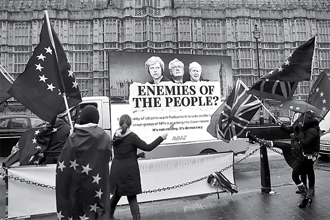  Penunjuk perasaan pro-EU anti-Brexit melambai bendera Union dan EU di hadapan papan iklan memaparkan wajah May, Davis dan Setiausaha Luar Negeri Britain Boris Johnson di luar Dewan Rakyat di tengah London kelmarin. — Gambar AFP