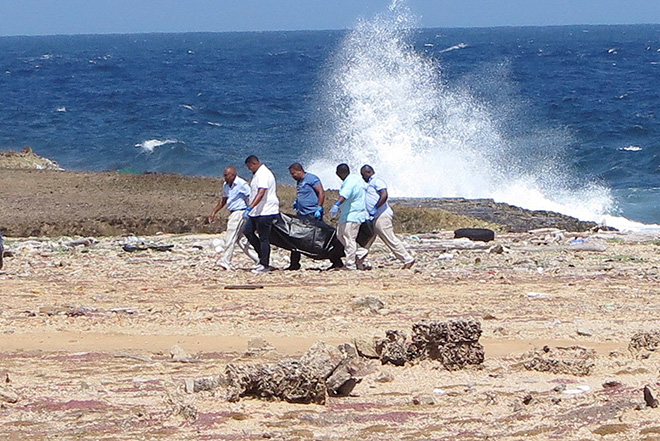  Pegawai forensik mengangkat beg mengandungi mayat yang ditemui di pantai,                          dekat Willemstad, Curacao, selepas bot membawa pendatang Venezuela karam. — Gambar Reuters/AFP