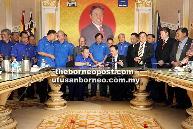  Abang Johari (tengah) menyaksikan Dr Sim (duduk kiri) dan Wong menandatangani MoU semalam.