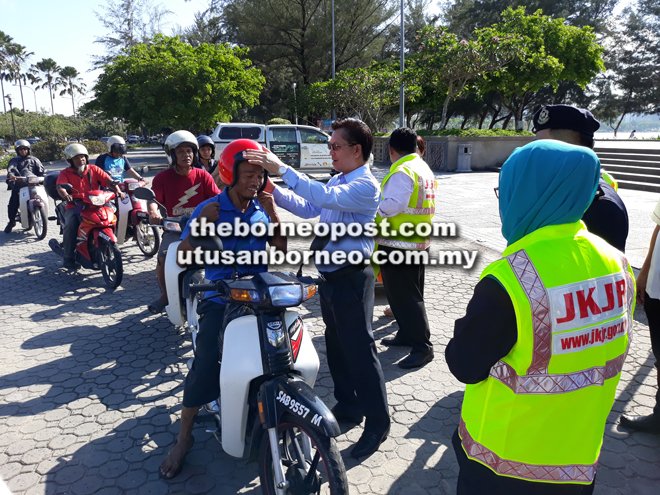  Joannes (tengah) memakaikan topi keledar kepada salah seorang penunggang motosikal.