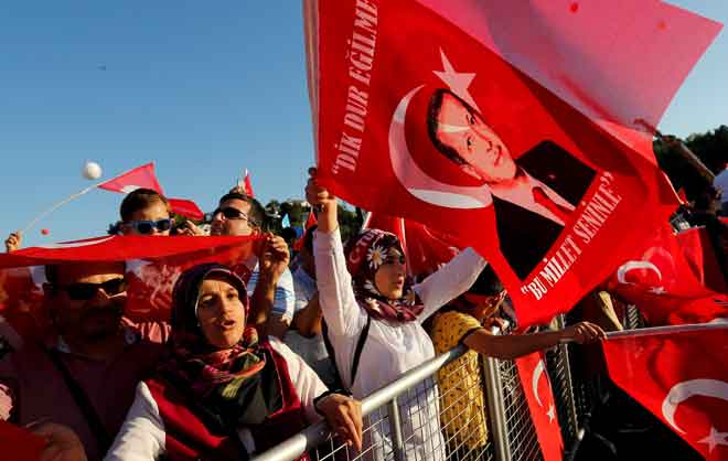  Orang ramai menjulang bendera Turki dan potret Erdogan ketika menghadiri upacara untuk menandakan ulang tahun kedua cubaan kudeta di Jambatan Bosphorus di Istanbul, Turki pada 15 Julai lalu. — Gambar Reuters