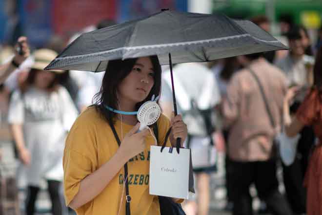  Seorang wanita menggunakan kipas angin kecil untuk menyejukkan badannya di Tokyo semalam akibat gelombang haba ‘luar biasa’ melanda Jepun sejak awal bulan ini. — Gambar AFP