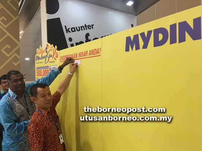  Rethnasamy dan Sutaghani (kanan)  menampal ikrar merdeka pada Kempen MyPledge di di Pasar Raya Besar MYDIN Petra Jaya, semalam.