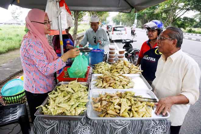  Peniaga ketupat Jamilah (kiri) melayan pelanggan yang ingin mendapatkan ketupat daun palas di gerainya. — Gambar Bernama