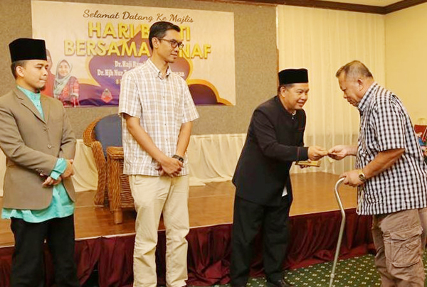 DR RAMLI menyerahkan sumbangan kepada salah seorang asnaf sambil diperhatikan Ustaz Saifuddin (dua kiri) dan Ustaz Ahmad (kiri).