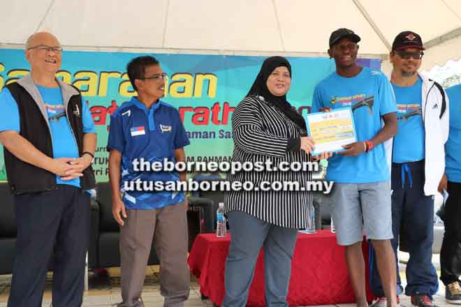  Rubiah (tengah) menyampaikan replika cek kepada Njihia sambil disaksi Ibrahim (kanan) dan Minos (kiri) pada larian Samarahan Half Marathon 2018 semalam. 