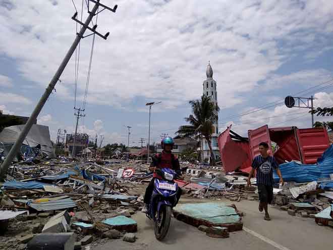  Penduduk tempatan membuat laluan di sepanjang jalan yang penuh dengan serpihan setelah gempa bumi dan tsunami melanda Palu di Pulau Sulawesi, semalam. — Gambar AFP