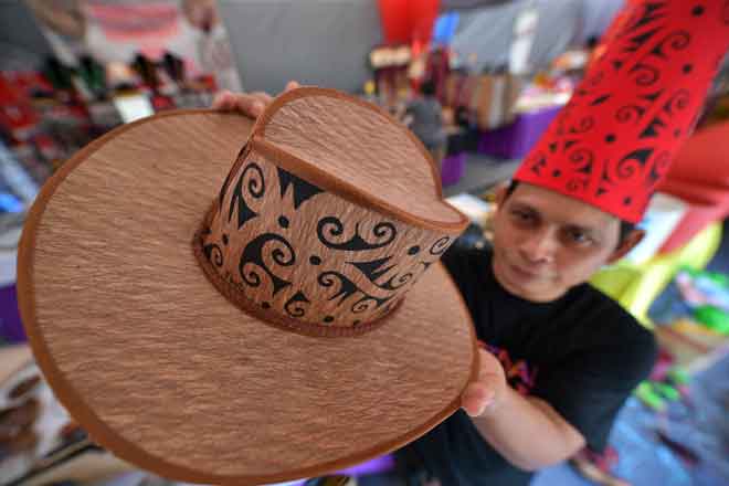  Albot  menunjukkan hasil lukisan corak motif Sarawak pada topi yang diperbuat daripada kulit kayu dengan hanya menggunakan sebatang pemberus lukisan dan dakwat hitam di Festival Kraf Sarawak semalam. — Gambar Bernama