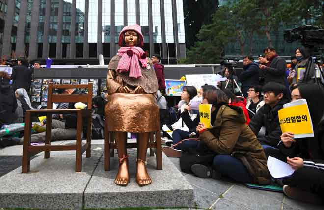  Penunjuk perasaan di Korea Selatan duduk dekat sebuah patung seorang  gadis remaja yang melambangkan bekas ‘wanita selesa’ sewaktu demonstrasi anti-Jepun mingguan                                                                    di hadapan kedutaan Jepun di Seoul semalam. — Gambar AFP