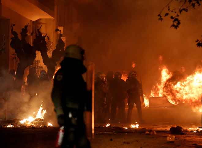  Polis rusuhan dilihat berdiri di antara api-api sewaktu tunjuk perasaan bagi      memperingati Grigoropoulos, di Athens kelmarin. — Gambar Reuters