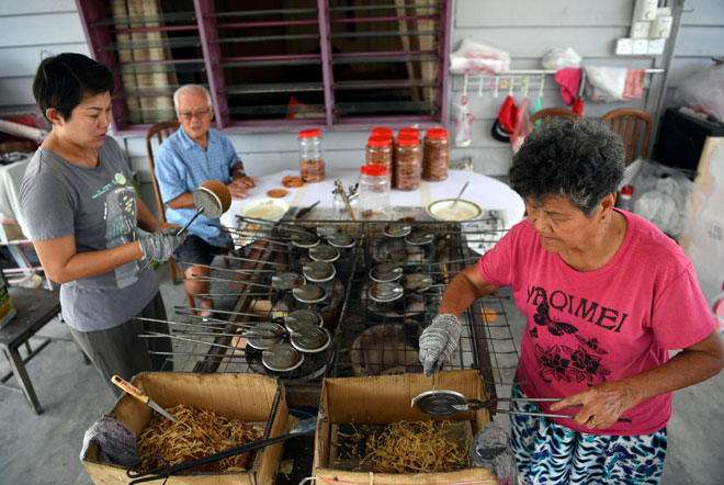  Choo dibantu ibunya, Fong dan ayahnya Choo membakar kuih kapit menggunakan dapur arang dalam menyiapkan tempahan pelanggan menjelang Tahun Baharu Cina di rumahnya di Kampung Sungai Lembing dekat Kuantan, baru-baru ini. — Gambar Bernama