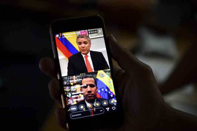  Seorang wartawan mengikuti perbualan secara langsung dalam talian antara Presiden Colombia Ivan Duque (atas) dan Guaido menerusi telefon pintar di Caracas kelmarin. Maduro mengecam AS kelmarin kerana ‘mencuri’ berbilion dolar dan memberi ‘sisa’ untuk bantuan kemanusiaan. — Gambar AFP