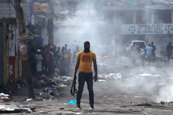  Seorang lelaki memegang senapang di sebelah penghadang yang dibakar semasa demonstrasi antikerajaan di Port-au-Prince, Haiti pada Ahad. — Gambar Reuters