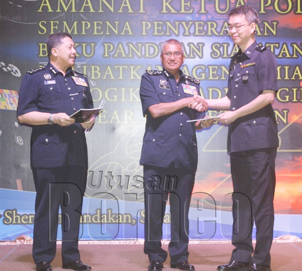 MOHD Fuzi (tengah) menyerahkan Buku Panduan Siasatan Jenayah CBRNE kepada salah seorang KBSJD dalam satu majlis di Sandakan.