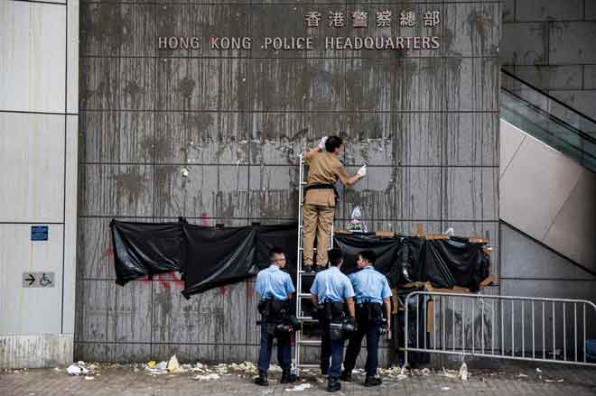  Seorang pencuci mengikis tanda sementara anggota polis berdiri di depan grafiti yang ditutup pada dinding di luar ibu pejabat polis di Hong Kong, semalam. — Gambar AFP