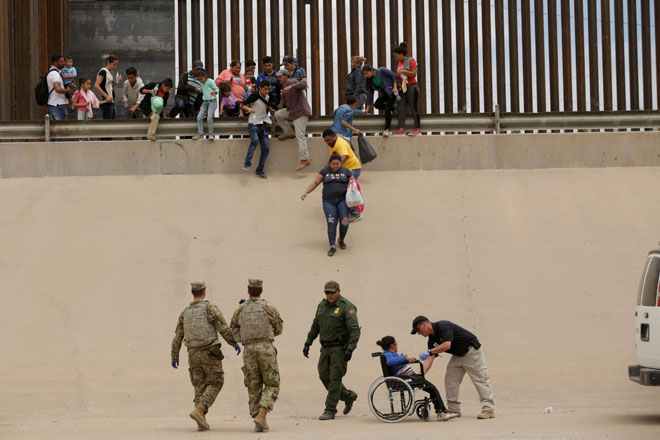  Anggota Pengawal Sempadan dan tentera AS membantu seorang wanita migran yang berkerusi roda ketika beliau dan pendatang lain merentasi sempadan antara AS dan Mexico untuk memohon suaka politik, seperti yang dapat dilihat dari Ciudad Juarez, kelmarin. — Gambar Reuters