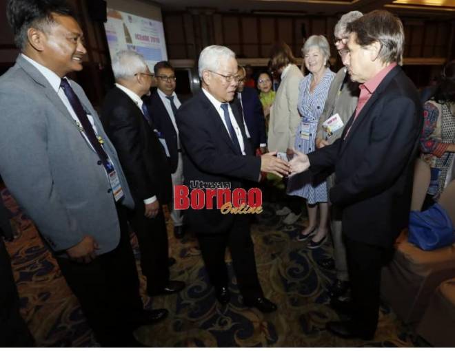 Manyin berjabat tangan dengan peserta persidangan sebaik tiba bagi majlis perasmian di Kuching hari ini. Gambar Chimon Upon