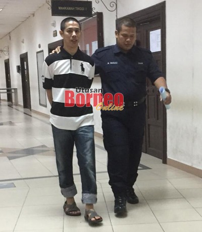 Izrol ketika diiring polis ketika menuju ke bilik tahanan Mahkamah Kuching hari ini.