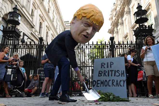  Seorang lelaki memakai topeng menyerupai Johnson, di sebelah nisan olok-olok dengan perkataan ‘Bersemadi Dengan Tenteram Demokrasi British’, ketika menunjuk perasaan di luar Downing Street di tengah London kelmarin. — Gambar AFP