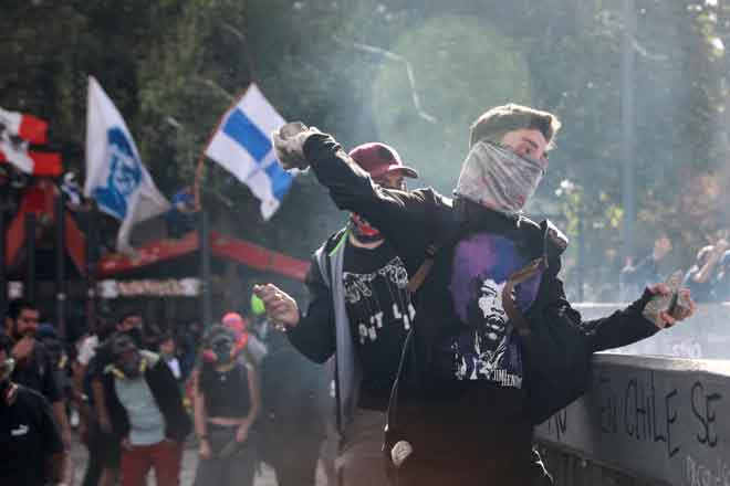  Penunjuk perasaan melontar batu ke arah anggota pasukan keselamatan semasa                 demonstrasi antikerajaan di Santiago, Chile kelmarin. — Gambar Henry Romero/Reuters  