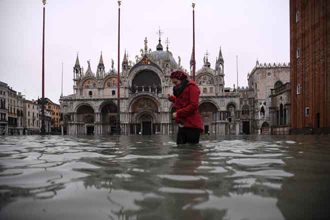  Seorang wanita dilihat meredah banjir di Dataran St Mark selepas air pasang tinggi melanda Venice, Itali semalam. — Gambar Marco Bertorello/AFP