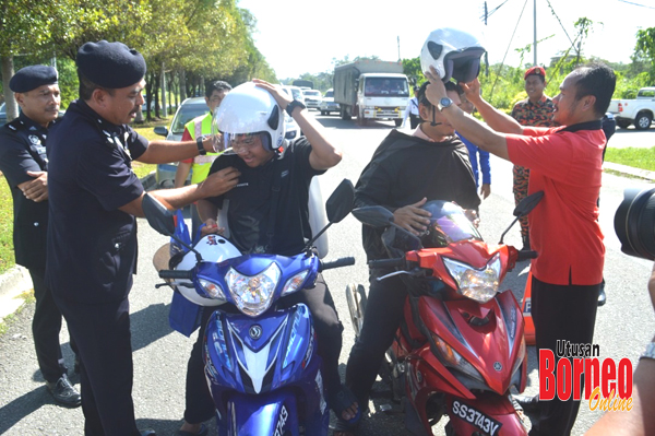  Abdul Fuad (kiri) dan Penolong Pegawai Tadbir JKJR Sabah Zunaide Mohd Ali (kanan) memakaikan topi keledar kepada penunggang motosikal.