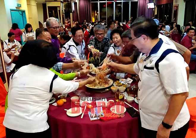  Dr Annuar (tengah), Lau (lima kiba) enggau raban ke bukai lebuh ti ngirau ‘Yee Sang’ ba Pengerami Makai Lemai Taun Baru China Serakup KMKK China Pampang Sibu, apin lama ti udah.