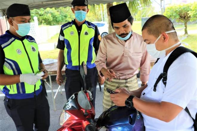 Aizat bersama pengawal masjid memeriksa kod QR jemaah yang hadir sebelum dibenarkan masuk.