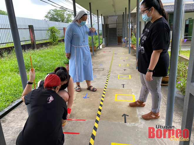 Rowena (dua kanan) bersama Hanna (kanan) turut memantau kakitangan sekolah yang mempersiapkan tanda laluan masuk dan keluar kepada kanak-kanak tadika yang memulakan sesi sekolah esok.