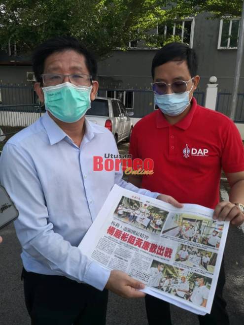 Julian (kiri) dan Anthony menunjukkan keratan akhbar yang memaparkan acara di mana berlakunya penyerahan bendera parti serta poster seakan kertas mengundi.