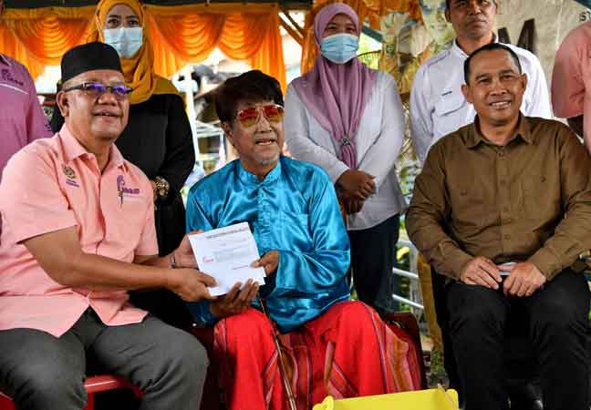 Zakaria (kiri) menyampaikan sumbangan kepada M Daud Kilau (tengah) pada Program Ziarah Finas Prihatin di kediamannya di Kampung Sungai Balai Baruh pada Jumaat lepas. — Gambar Bernama