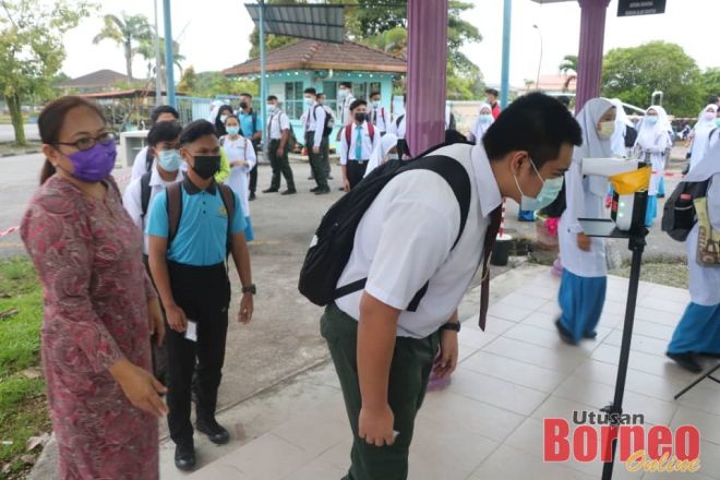 Pelajar SMK Kota Samarahan mengimbas suhu badan sebelum masuk ke sekolah.