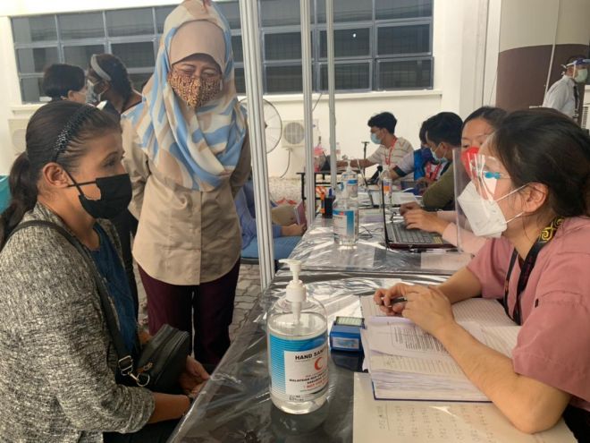 Fatimah (tengah) melihat sendiri proses pemberian vaksin kepada seorang gelandangan di PPV Stadium Perpaduan Sarawak, hari ini.