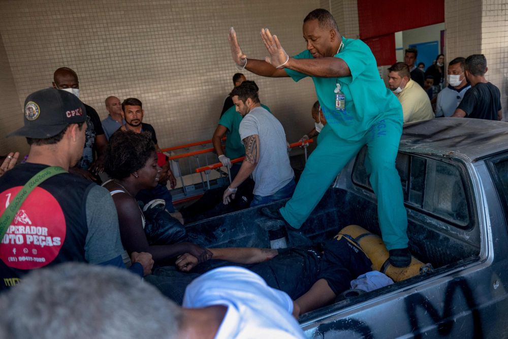 Seorang wanita memegang tangan mangsa yang terbaring di belakang trak di Hospital Getulio Varas selepas serbuan polis di favela di Rio de Janeiro kelmarin. - Gambar AFP