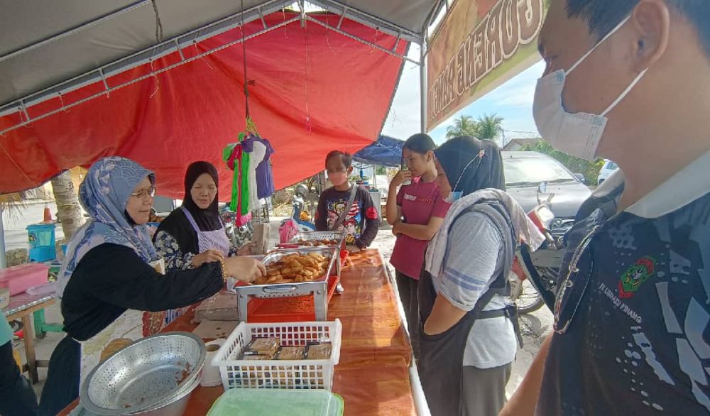 Armah (kiri) melayan pelanggan yang datang ke gerainya untuk membeli pisang goreng rangup.