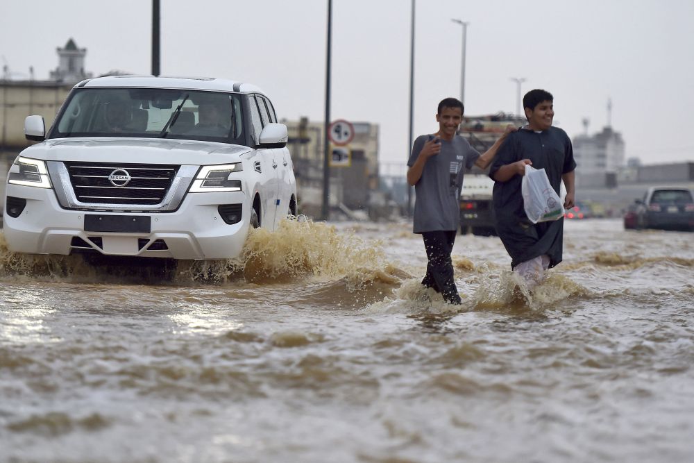 Dua lelaki dilihat melintasi jalan raya yang ditenggelami banjir ekoran hujan lebat di bandar Jeddah kelmarin. — Gambar AFP