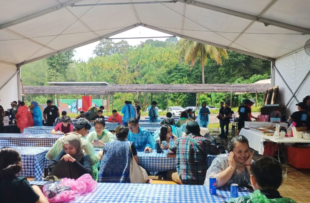 Pengunjung makan dengan masih memakai baju hujan sementara menunggu berhentinya hujan sebelum meneruskan menonton konsert festival yang berlangsung di Sunbear Stage.